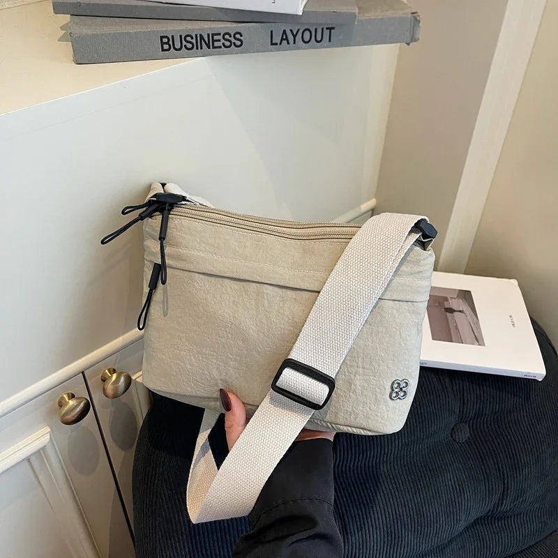 Minimalist beige crossbody bag with adjustable strap on black chair near wall and books