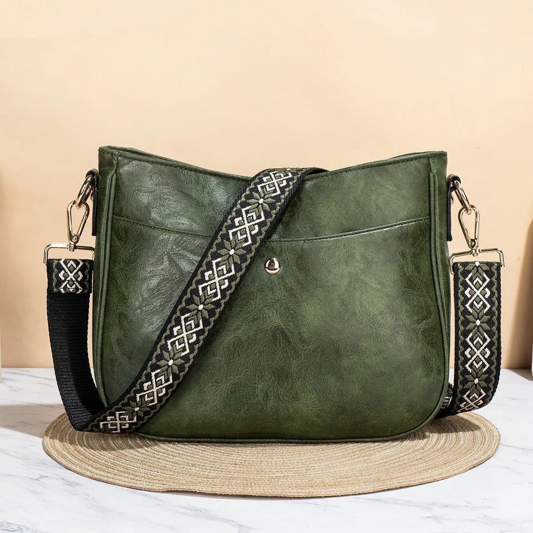 Green leather crossbody bag with patterned black and white strap on round woven mat