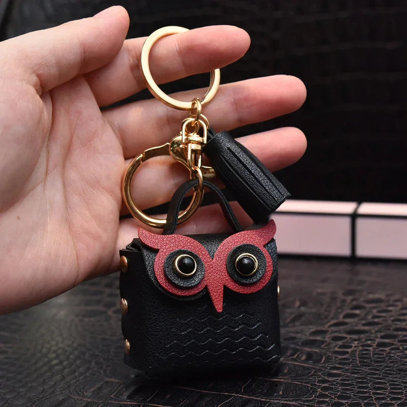 Hand holding black leather owl keychain with gold ring and black tassel on textured surface