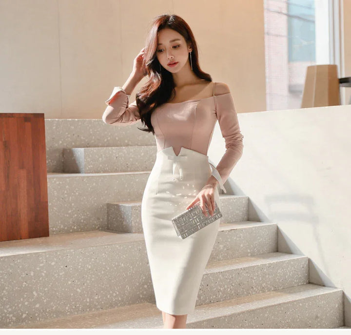 Woman in beige off-shoulder top and white pencil skirt holding silver clutch on indoor stairs