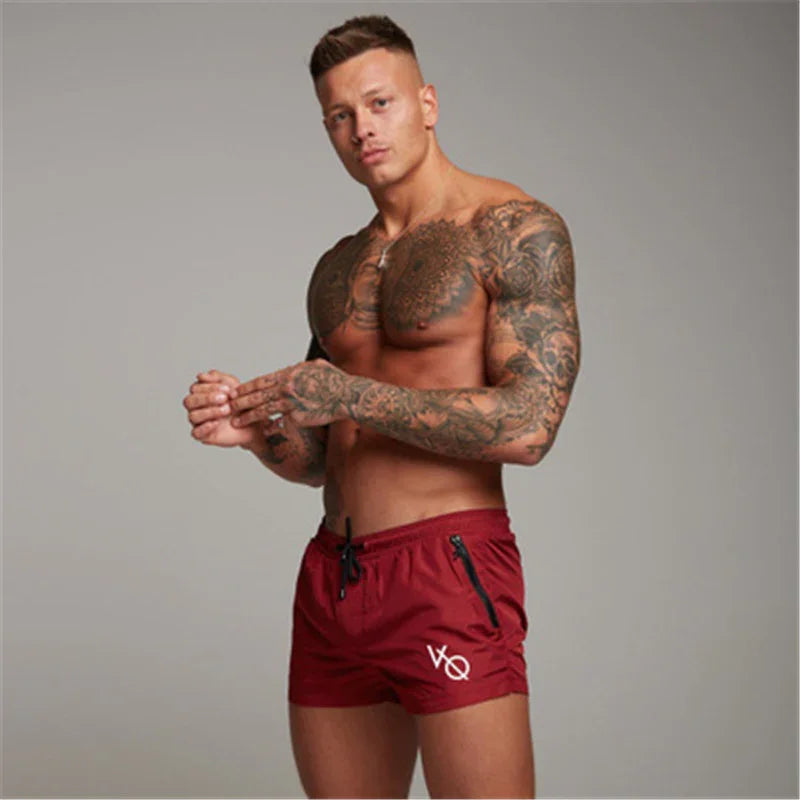 Tattooed muscular man in red workout shorts posing against gray background