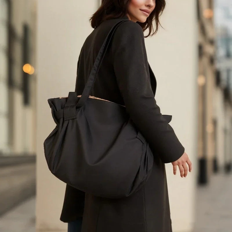 Woman wearing black coat carrying large black shoulder bag in urban setting