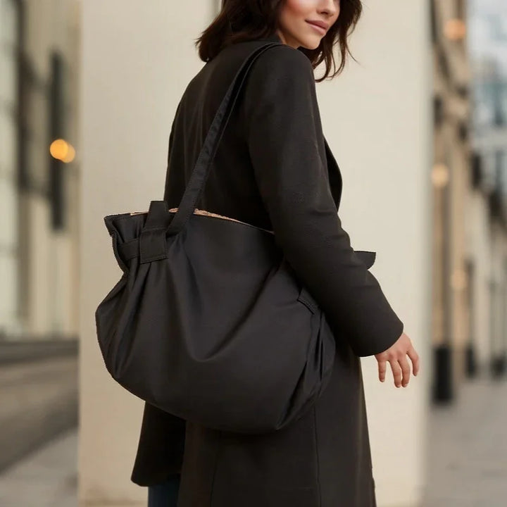 Woman wearing black coat carrying large black shoulder bag in urban setting