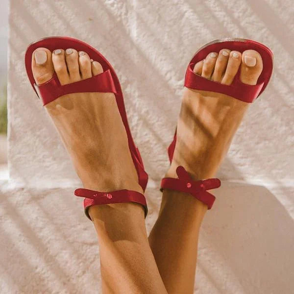Close-up of feet wearing stylish red strappy sandals with ankle straps against a light background