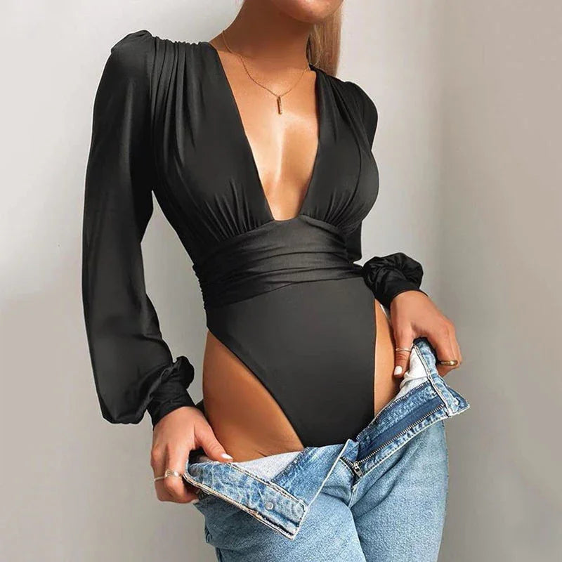 Woman wearing black long-sleeve deep V-neck bodysuit with high-cut legs, pulling down light blue jeans