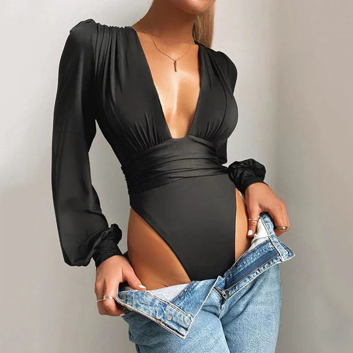 Woman wearing black long-sleeve deep V-neck bodysuit with high-cut legs, pulling down light blue jeans