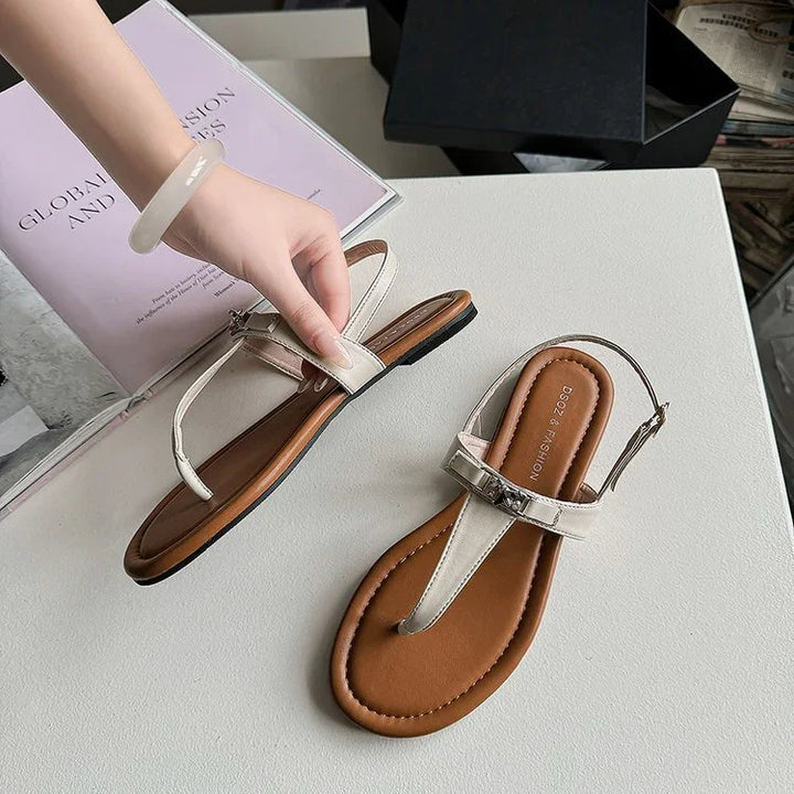 Pair of stylish beige thong sandals with brown cushioned soles on white surface, hand holding one sandal