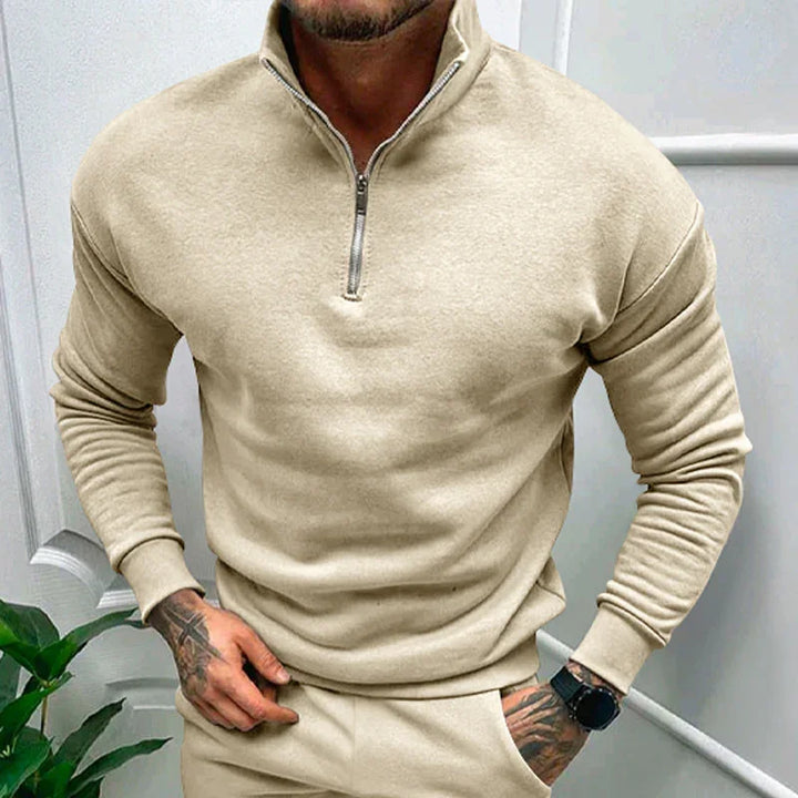Man wearing beige half-zip sweater and matching pants with tattooed hands and smartwatch