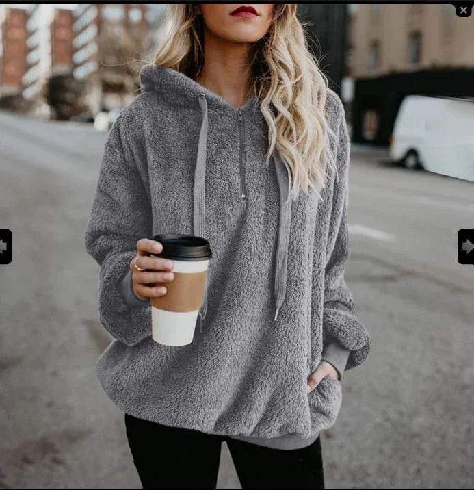 Woman wearing cozy gray sherpa fleece hoodie holding a takeaway coffee cup in urban street setting