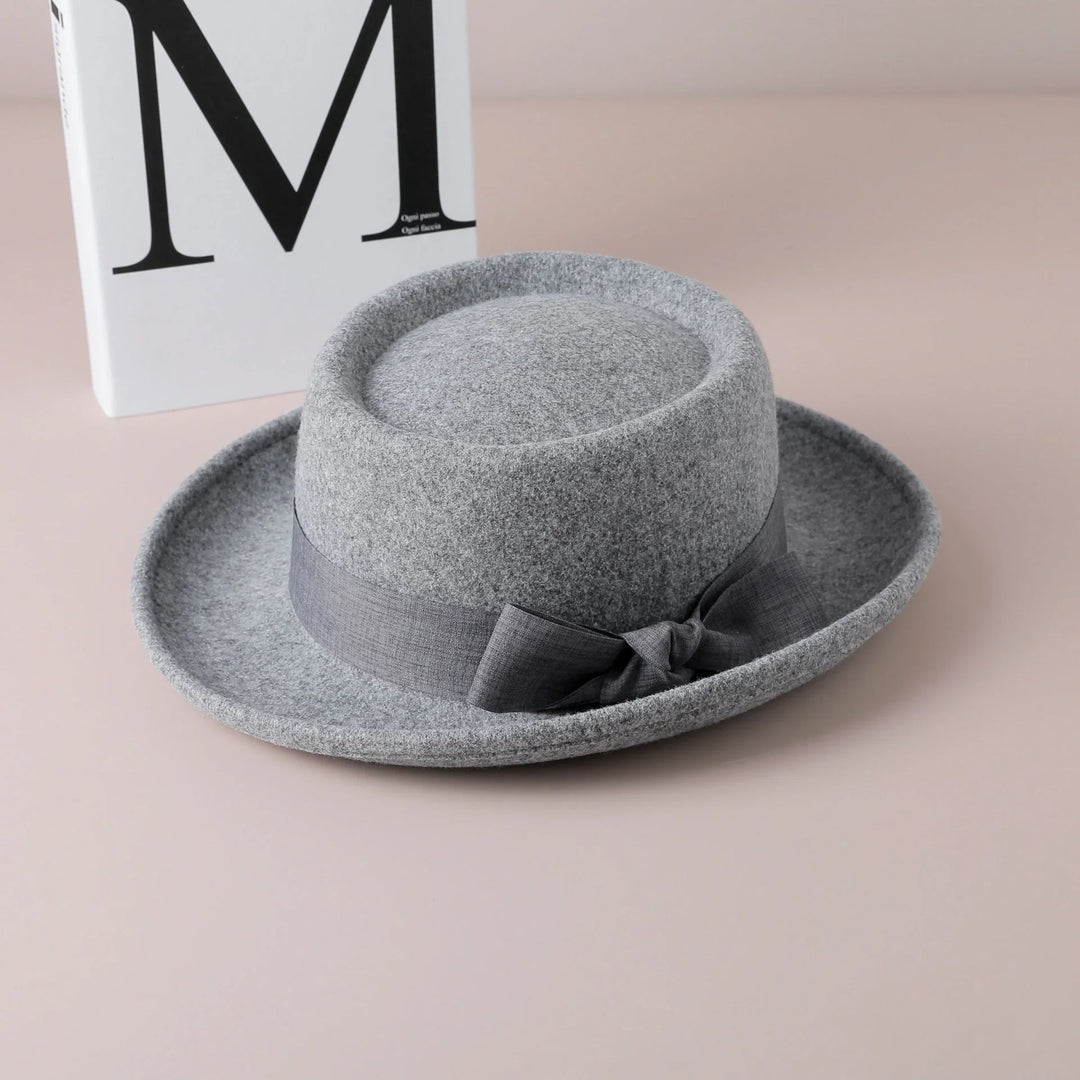 Gray felt fedora hat with dark gray ribbon bow on beige surface with white book background