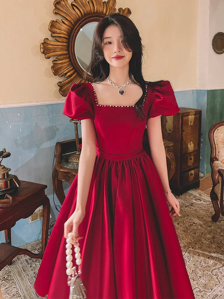 Woman in elegant red puff sleeve dress holding pearl handle purse in vintage styled room