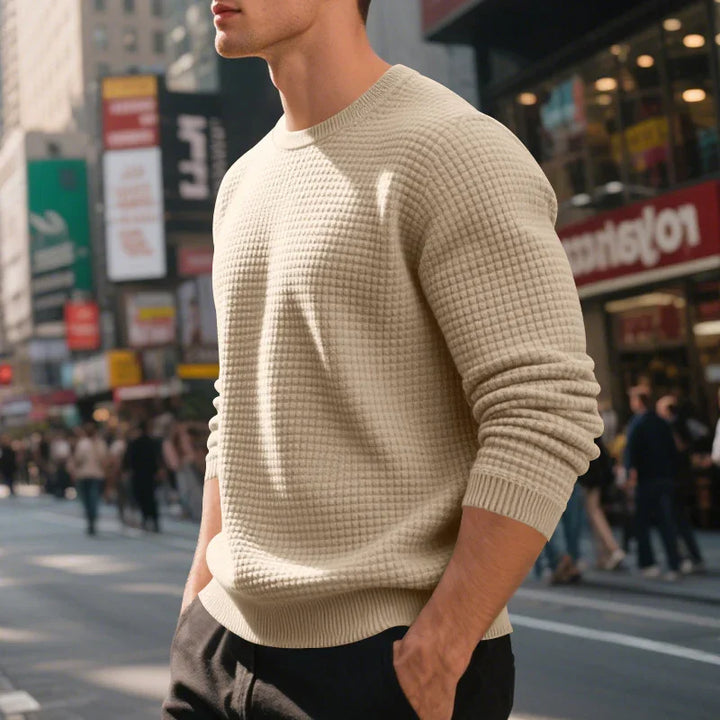 Man wearing beige waffle knit sweater with hands in pockets on busy city street