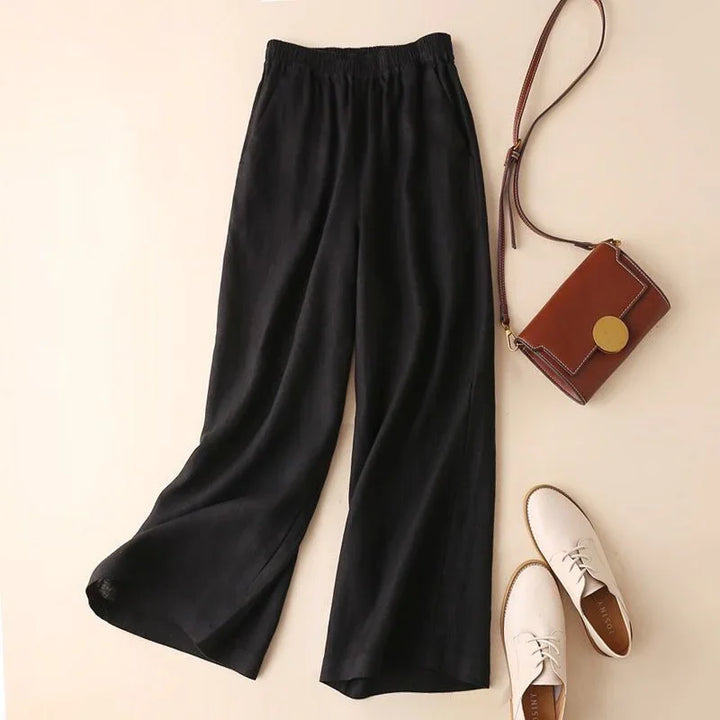 Black wide-leg pants with elastic waist, brown crossbody bag, and white lace-up shoes on beige background