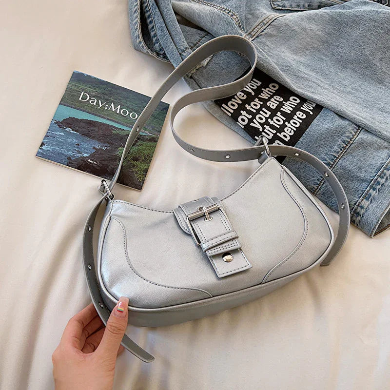 Silver leather shoulder bag with buckle detail, light blue denim jacket, and square photo card on white surface