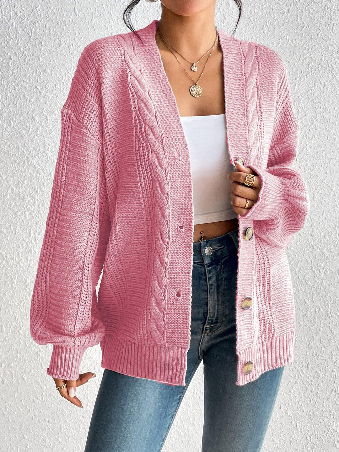 Woman wearing oversized pink cable knit cardigan with buttons, white crop top, and blue jeans