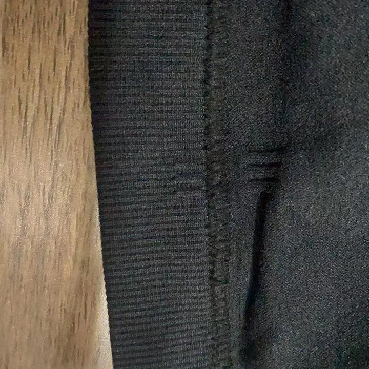 Close-up of black ribbed fabric and seam detail next to brown wooden surface