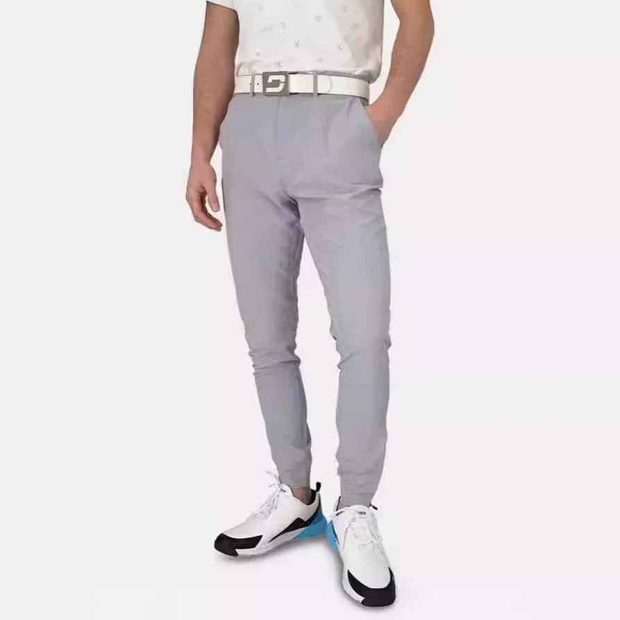 Man wearing light gray slim jogger pants with white belt and white sneakers with black and blue accents