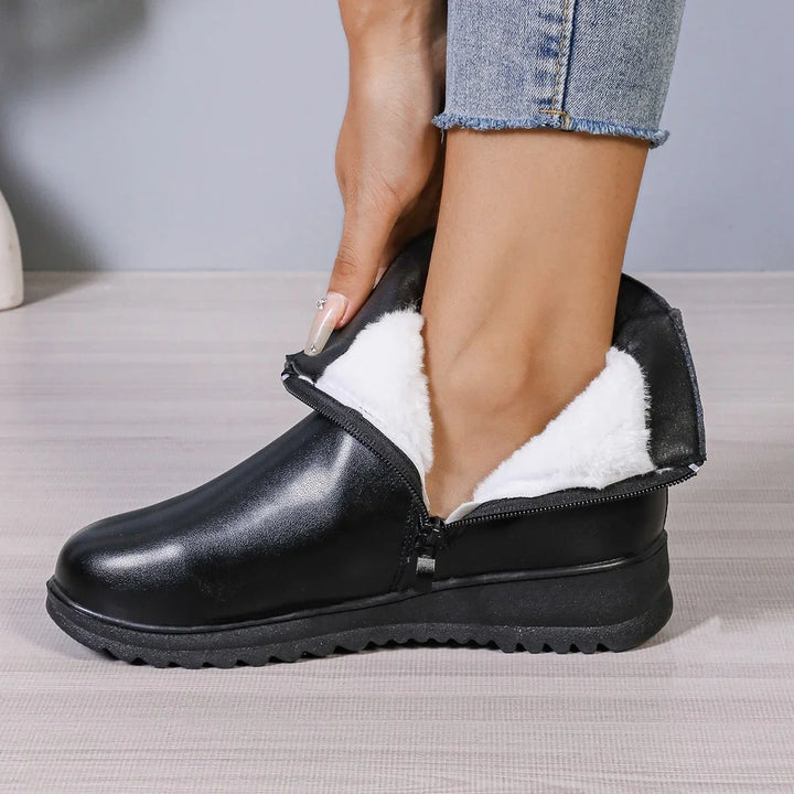 Black winter boots with white faux fur lining and zipper worn with rolled-up jeans on wooden floor