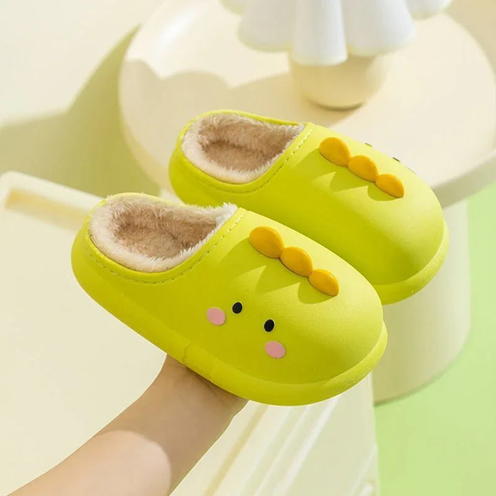 Hand holding yellow plush-lined indoor slippers with cute face and orange buttons on top