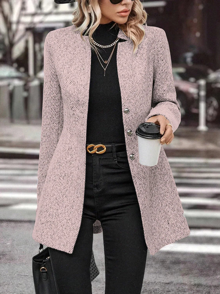 Woman wearing pink textured blazer, black turtleneck and pants, holding coffee cup on city street