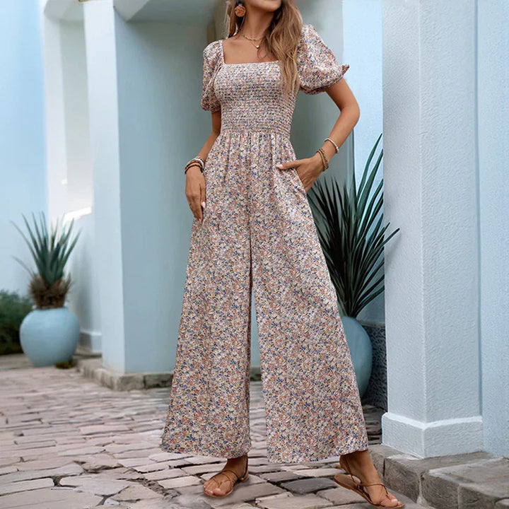 Woman wearing floral puff sleeve wide-leg jumpsuit with square neckline and sandals, standing outdoors