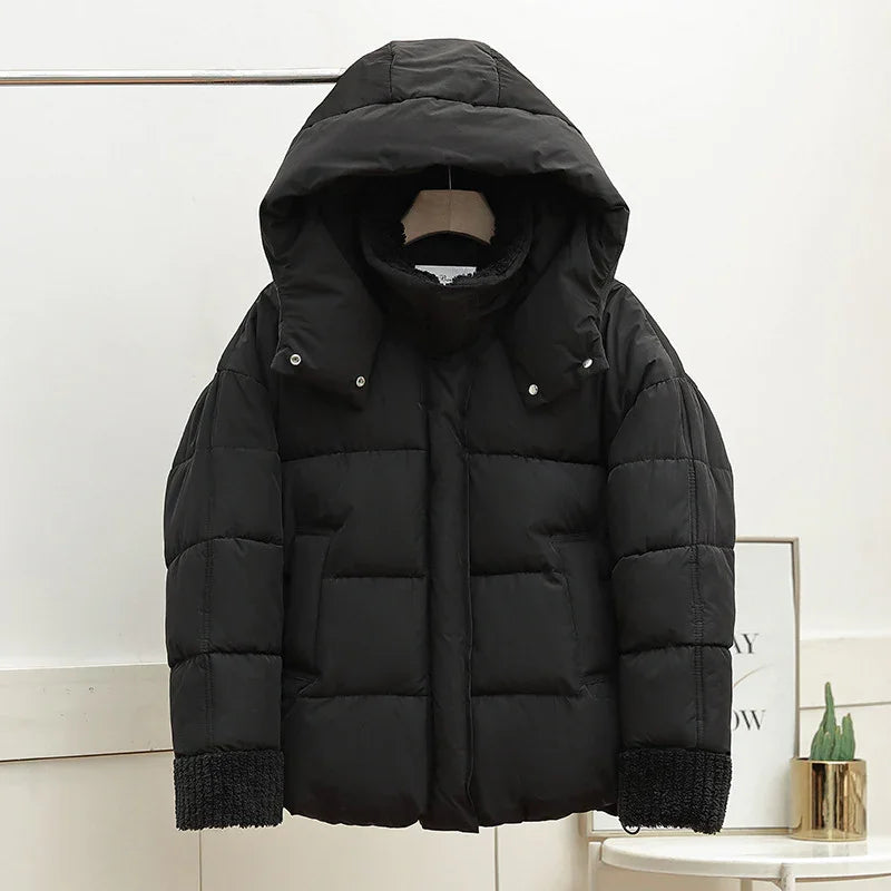 Black puffer jacket with large hood and knit cuffs hanging on a rack in a minimalist room