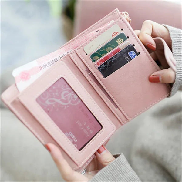 Hands holding an open pink leather wallet with multiple card slots and cash inside