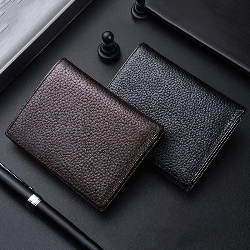 Two textured leather wallets, one brown and one black, placed on a black surface with a pen and chess pawns