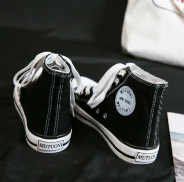 Pair of black high-top canvas sneakers with white laces and MUTUONI branding on a black surface