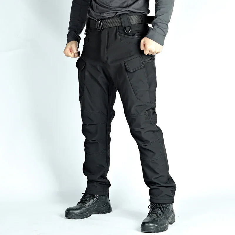Man wearing black tactical pants with cargo pockets and black boots against white background