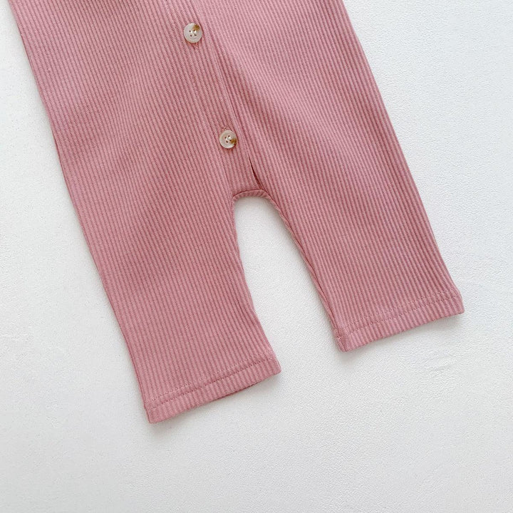 Close-up of pink ribbed fabric baby romper legs with two beige buttons on white background