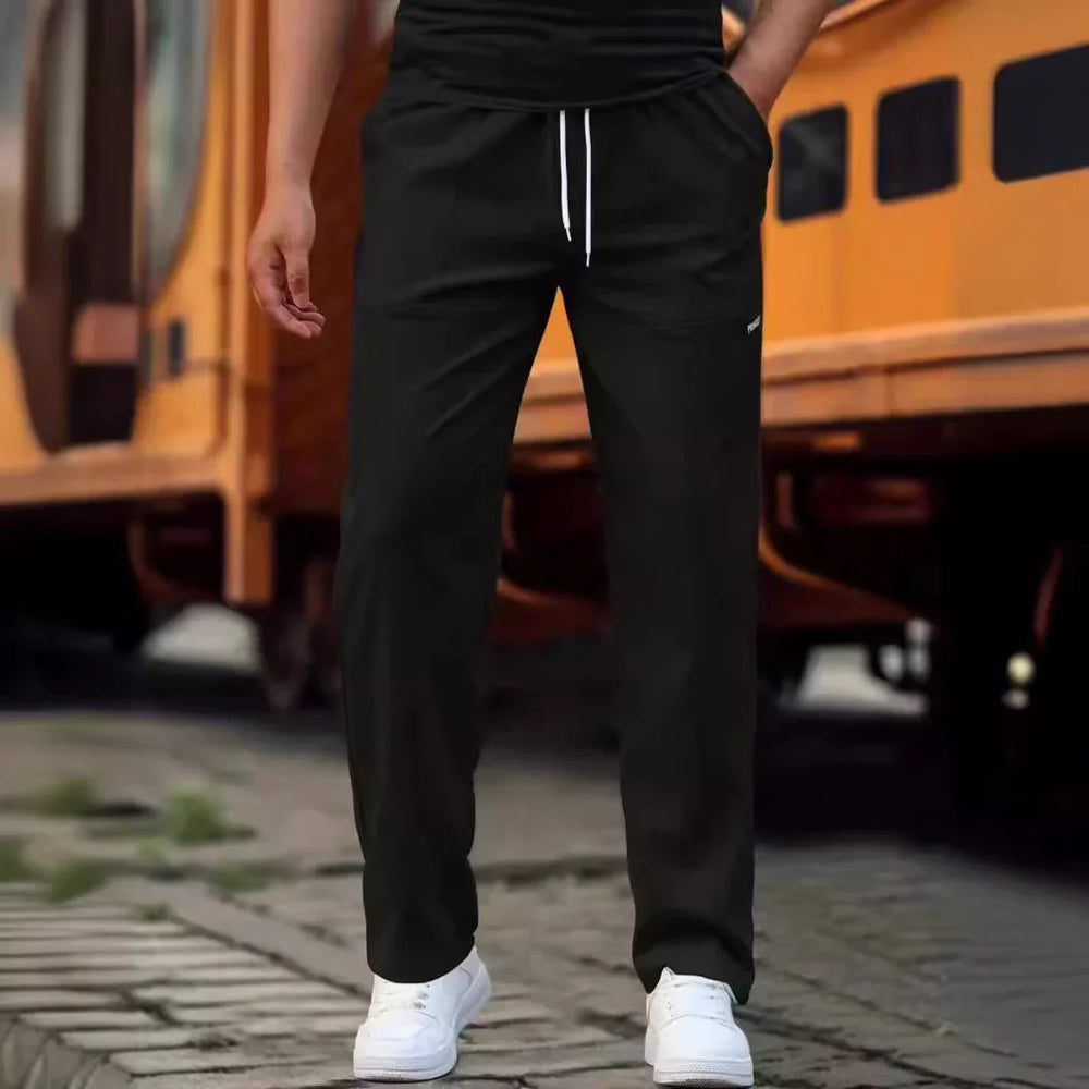 Man wearing black jogger pants with white drawstrings and white sneakers beside yellow train