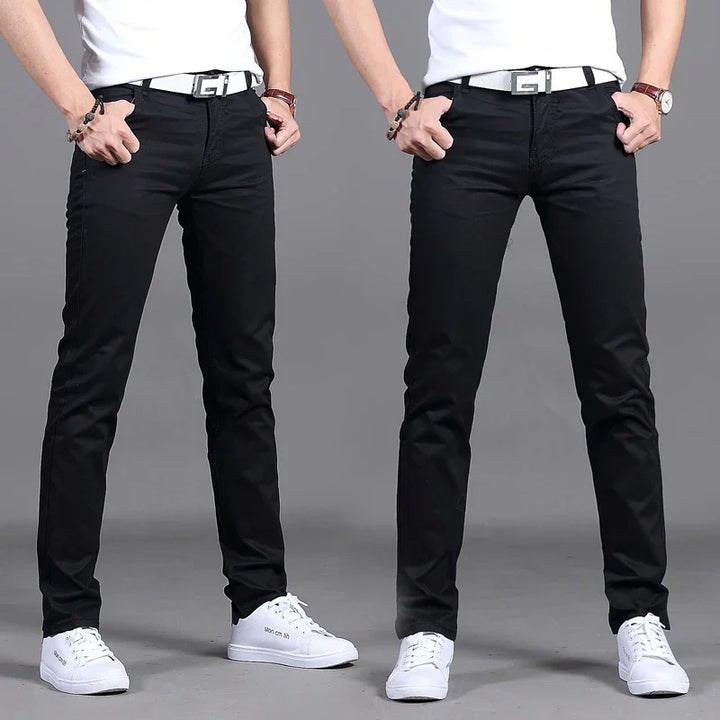 Man wearing black slim-fit pants with white belt and white sneakers against gray background