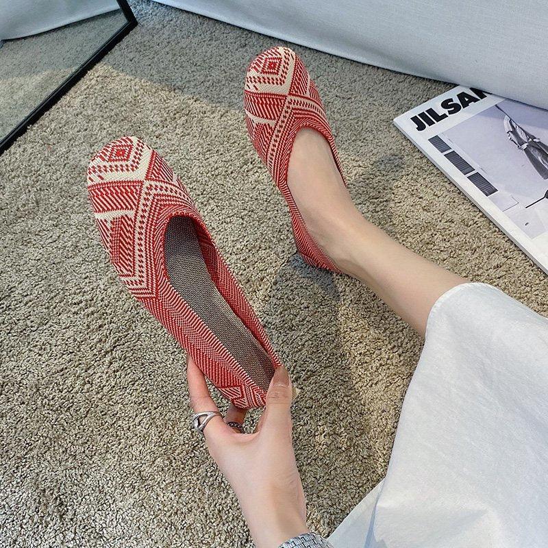 Pair of red and white patterned flat shoes on feet and hand over carpet with fashion magazine