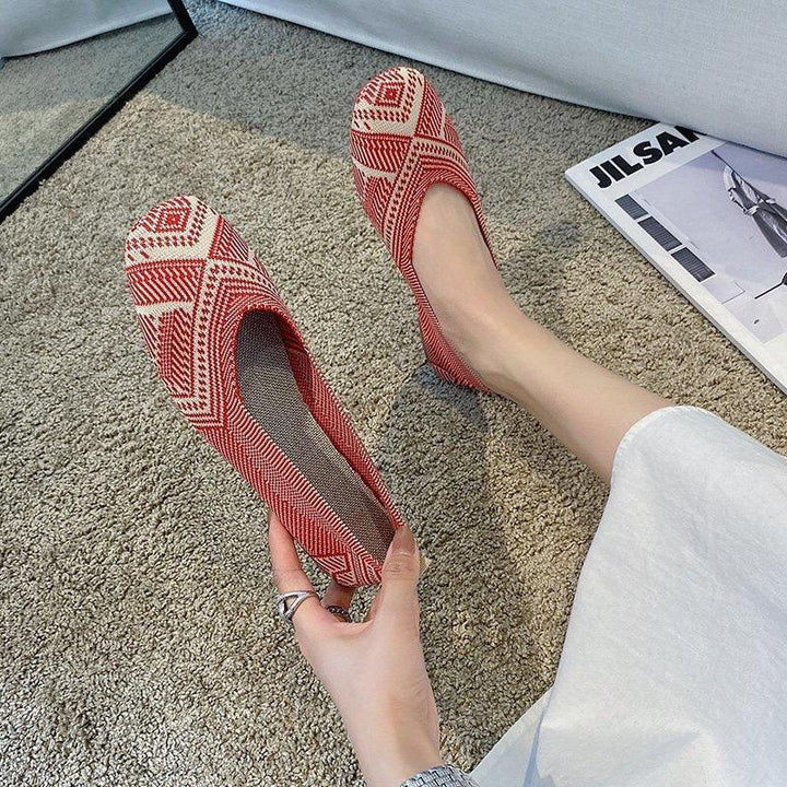 Pair of red and white patterned flat shoes on feet and hand over carpet with fashion magazine