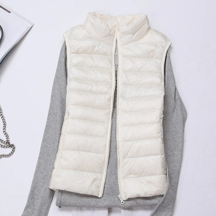 White quilted sleeveless puffer vest layered over long-sleeve gray sweater on white background