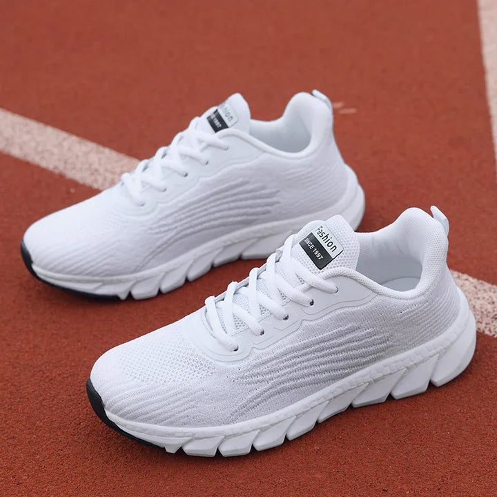 Pair of white lightweight running shoes with textured sole on red track surface