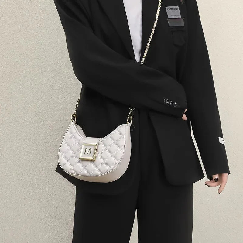 Woman wearing black suit holding white quilted handbag with gold chain strap and 'M' clasp