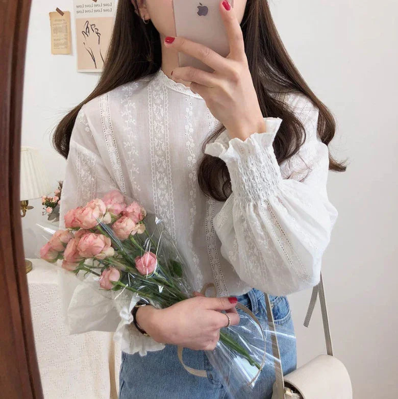 Woman in white lace blouse holding pink roses bouquet and smartphone, casual denim jeans outfit