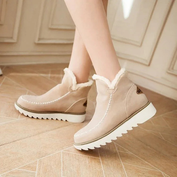Beige suede winter ankle boots with white faux fur lining and chunky white ridged sole on wooden floor