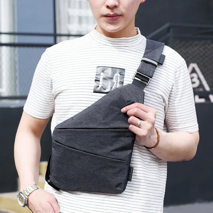 Man wearing striped shirt and gray crossbody sling bag outdoors, urban background
