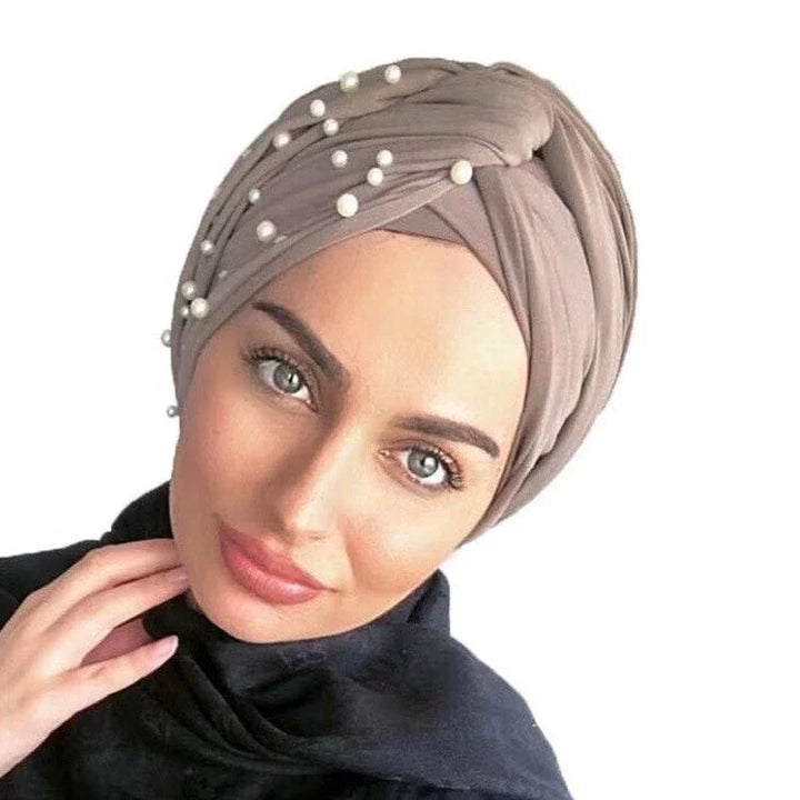 Woman wearing taupe turban headwrap adorned with white pearls and black top, close-up portrait