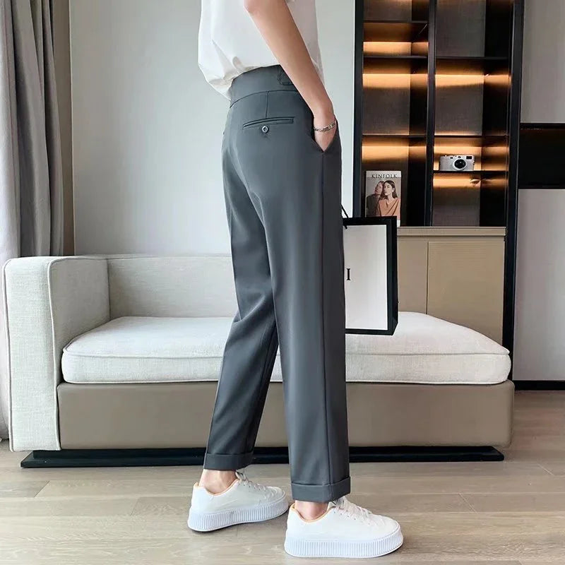 Person wearing gray tailored pants and white sneakers standing in a modern living room