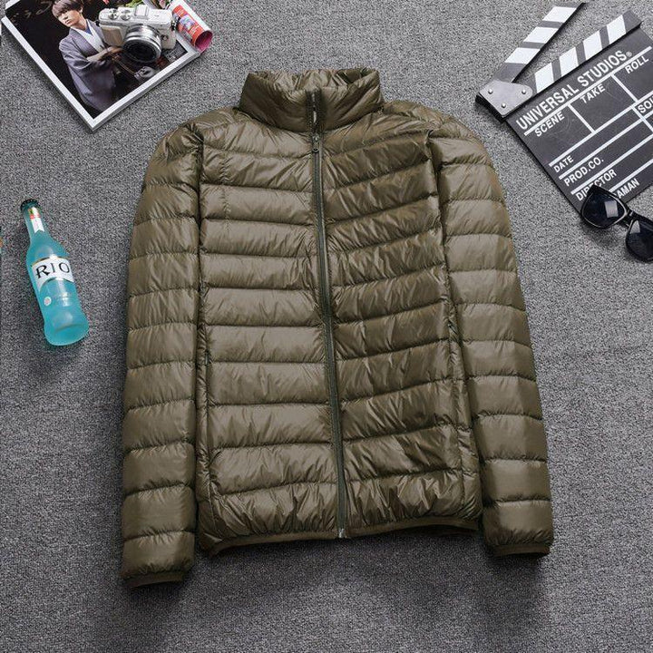 Olive green lightweight puffer jacket laid flat on gray carpet with magazine, blue drink bottle, sunglasses, and film clapperboard