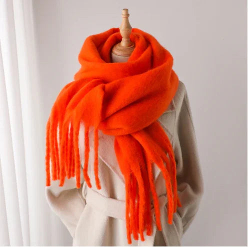 Bright orange fringed wool scarf wrapped on cream coat mannequin in minimalist setting