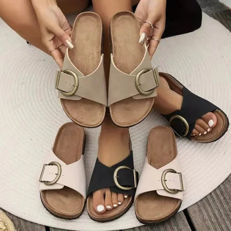 Woman wearing black buckle slide sandals holding beige buckle slide sandals on round rug