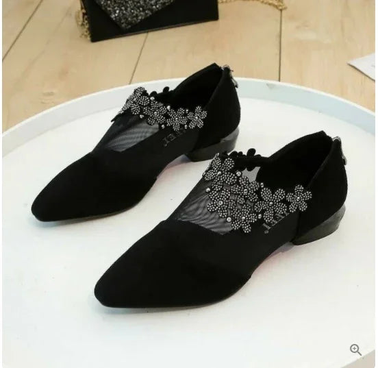 Black pointed toe flats with floral lace and bead embellishments on mesh uppers on white surface