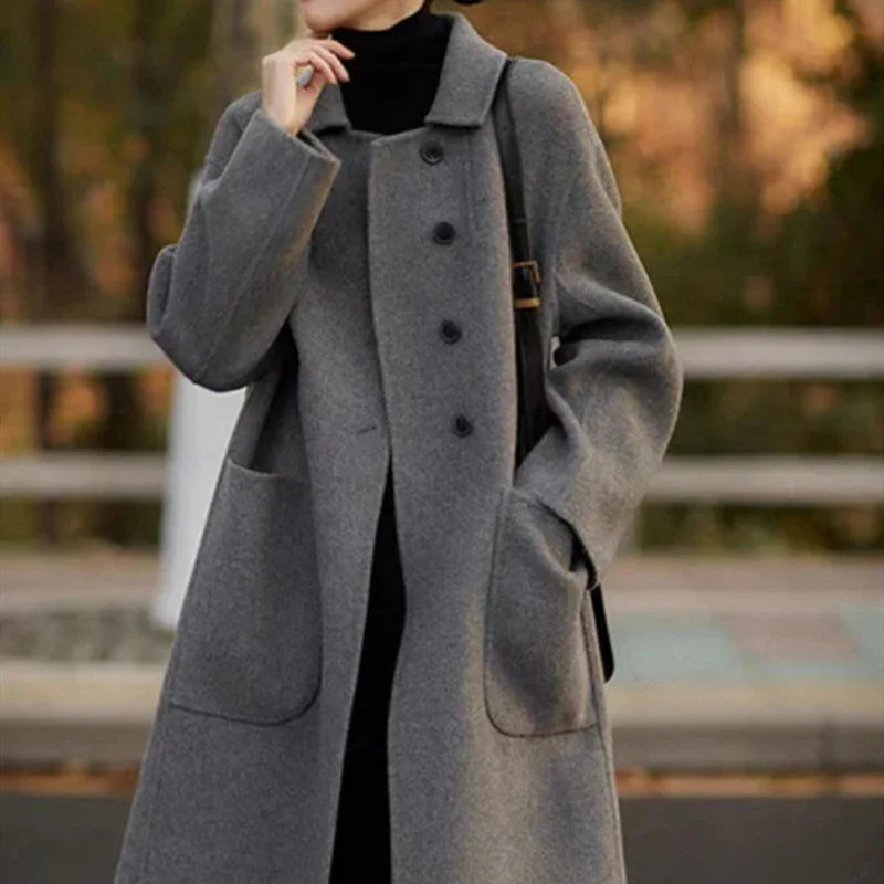 Woman wearing long gray buttoned wool coat with pockets over black turtleneck outside in autumn