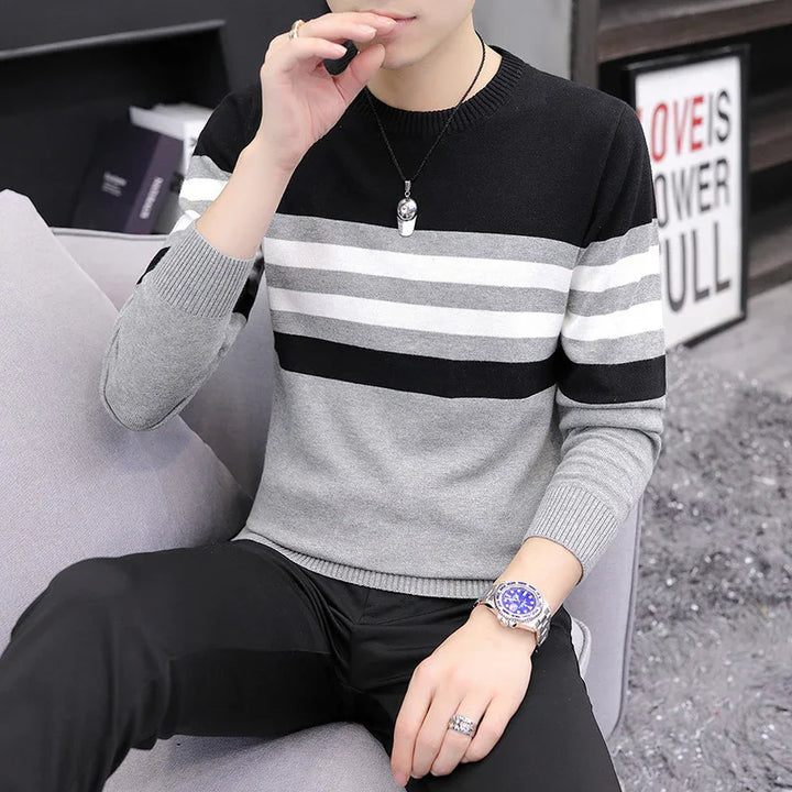 Man wearing black gray white striped sweater, black pants, silver watch and ring, sitting on gray couch