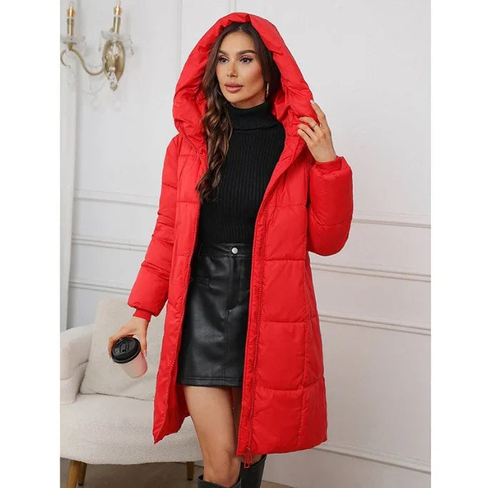 Woman wearing a red hooded puffer coat over a black turtleneck and leather skirt indoors